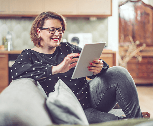 A woman sitting in her lounge on a couch using her tablet