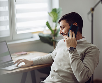 A man talking on the phone while using his laptop